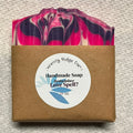 Handmade soap bar with a colorful swirl pattern in a brown box on a textured surface.